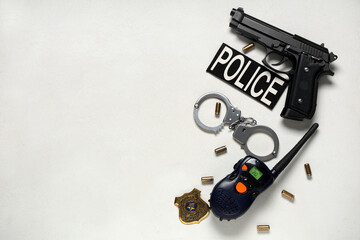 Police officer's handcuffs, gun, bullets, walkie-talkie and shield on light background