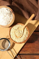 Brown rice, flour and sieve on wooden table, flat lay