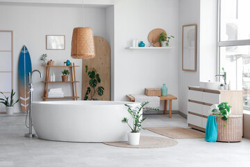 Interior of light bathroom with bathtub, houseplants and surfboard