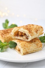 Pieces of tasty apple strudel and mint on white table, closeup