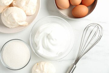 Delicious homemade meringue cookies, ingredients and whisk on white marble table, flat lay