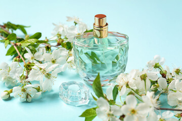 Bottle of aromatic perfume and twigs with beautiful flowers on light blue background, closeup