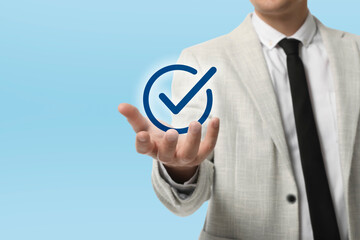Approved. Man holding virtual check mark in hand on light blue background, closeup