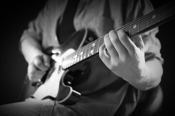 Man playing guitar in darkness, closeup. Black and white effect