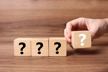 Woman holding cube with question mark at wooden table, closeup