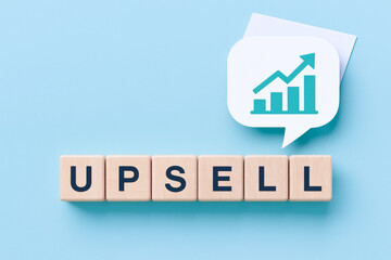 Fototapeta premium Upsell marketing concept with wooden blocks and upward graph icon on blue background showing business growth strategy