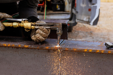 Welder is performing metal cutting with a torch, creating sparks at construction site under works day