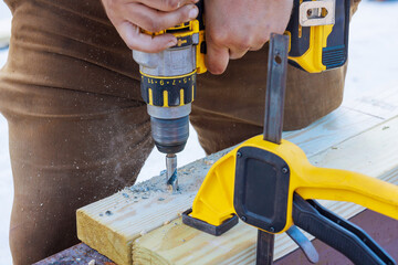 Skilled worker uses power drill to create holes in wooden beam at construction site during works day