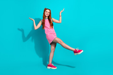 Naklejka premium Vibrant young woman posing in checkered summer dress against teal background, showcasing playful gestures and stylish fashion