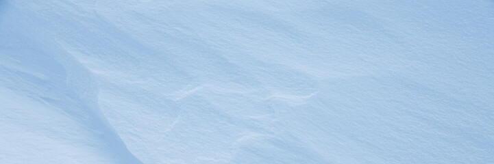 Beautiful winter background with snowy ground. Natural snow texture. Wind sculpted patterns on snow surface. Wide panoramic texture for background and design. Closeup top view with copy space.