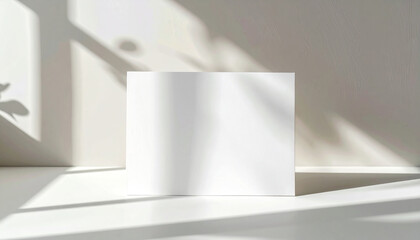 Empty white card or greeting card mockup with soft leaves shadows on neutral light grey concrete wall background