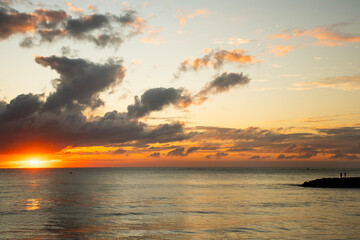 Sunrise on land facing the sea on a calm beach with clouds