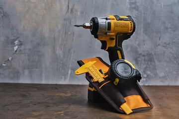 A tool belt holding a cordless drill, caliper, and tape measure lies on a worktable. Tools for construction and DIY projects.