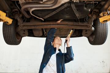 Woman, check and tool for service with auto in garage, inspection or maintenance on engine. Female mechanic, car and torch for problem with oil or motor, technician working or repair on transport