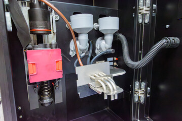 Close-up of internal mechanical components of an automatic coffee machine, showing pistons, powder dispensers, tubing and dispensing spouts.
