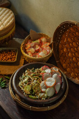 Authentic Sundanese karedok, raw vegetable salad with spicy peanut sauce, served with colorful crackers. Traditional Indonesian dish styled in rustic setup and natural light.