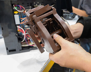 Technician holding brew group unit of coffee machine during maintenance with internal electronic components and wiring visible in background