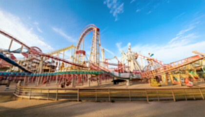 Obraz premium A blurred amusement park scene captures the essence of thrill and excitement, featuring a roller coaster against a backdrop of a bright blue sky. A blurred scenery to be used as background.