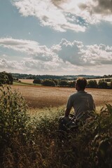 A busy farm under the bright sky with crops ready for harvest. A farmer is leaning on his tractor looking out over the fields. The mood is peaceful and proud