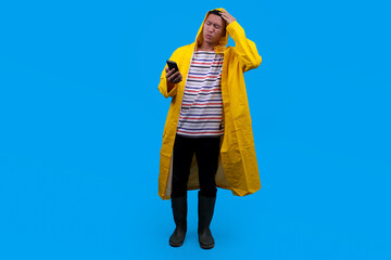 Confused Asian man in yellow waterproof raincoat outerwear use mobile cell phone while scratching head