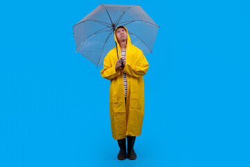Man in rain boots and cloak posing with umbrella against vibrant blue backdrop, full length view.