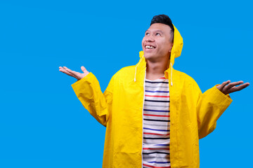 Happy boy in waterproof raincoat spreading arms to sides in rainy days isolated on blue background © Gatot