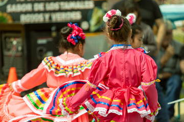 Little girls and other kids wearing traditional Mexican outfits during a cultural dance performance for Cinco de Mayo.