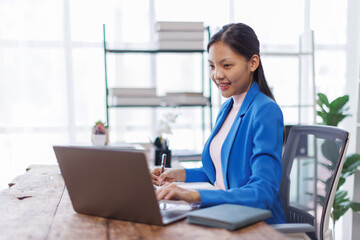 Brunette young asian businesswoman sitting at the office and using laptops for work. Confident professional female wearing business financial planning casual.