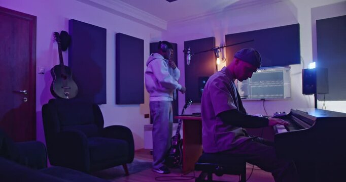 Music recording session with two musicians creating a new song. Singer practices with producer at electric piano.