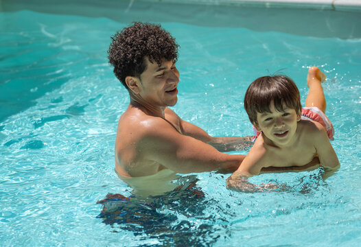 Smiling latin dad helping his son learning to swim in a home pool