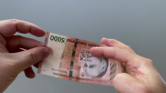 Horizontal 4K video. 60 fps. Cash money of Armenia. Man checking watermark with portrait of writer William Saroyan and pomegranate on 5000 dram. Male hand close up. Loan, debt, bribe, tax, pay, salary