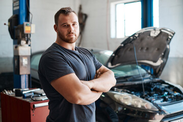 Mechanic, man and arms crossed by car in workshop for auto repair, service or safety in portrait....