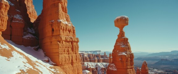 Towering hoodoos punctuate a tranquil mountain landscape, capped with a dusting of winter snow under a serene sky