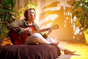 Woman playing acoustic guitar in a cozy room surrounded by indoor plants during golden hour light