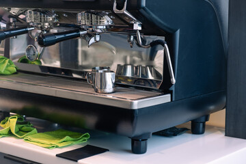 Close-up of a commercial espresso machine in a coffee shop featuring portafilters, a milk frothing jug, and cleaning cloths, highlighting its functionality and design in a cafe environment