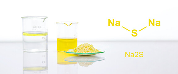 Sodium sulfide flake in Chemical Watch Glass place next to beaker on white laboratory table. The...