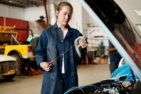 Car, dipstick and mechanic with woman in workshop for maintenance, repair or service of engine. Auto, expert and inspection with asian vehicle engineer or technician checking oil level in garage