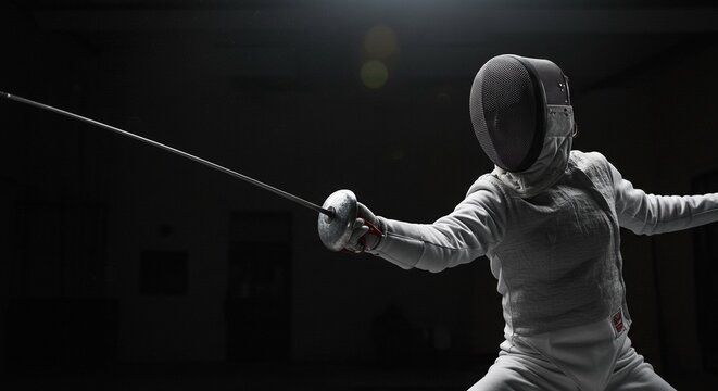 A fencer in white uniform and mask holding a foil in a dark room with a spotlight on the fencer
