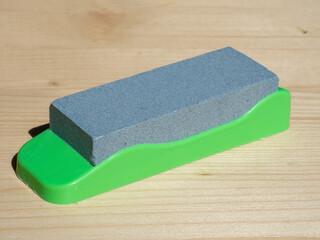 Sharpening stone with plastic base. Sharpening knives, scissors and chisels. Diamond grinding stone. Single grindstone or whetstone sharpener on wooden table
