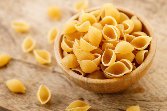 Raw uncooked dried Conchiglie shell pasta. Italian seashells pasta in wooden bowl on wooden background.