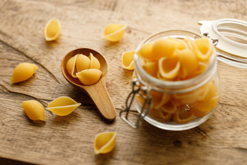 Raw uncooked dried Conchiglie shell pasta. Italian seashells pasta in lock lid glass jar on wooden background.