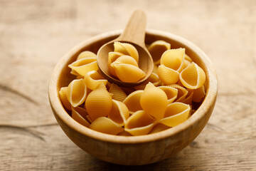 Raw uncooked dried Conchiglie shell pasta. Italian seashells pasta in wooden bowl on wooden background.