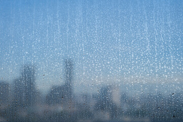 Raindrops on a glass window with a blurry cityscape in the morning background.