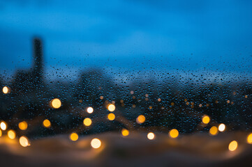 Raindrops on glass window with golden lights and blurred city background in bed room.
