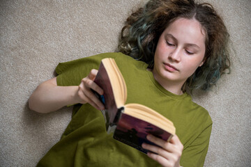 Teen age girl reading a book lying down on the floor