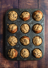 Top view of banana chocolate chip muffins in tin on wood table.