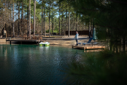 Man fishing on small dock by forest pond with lounge chairs