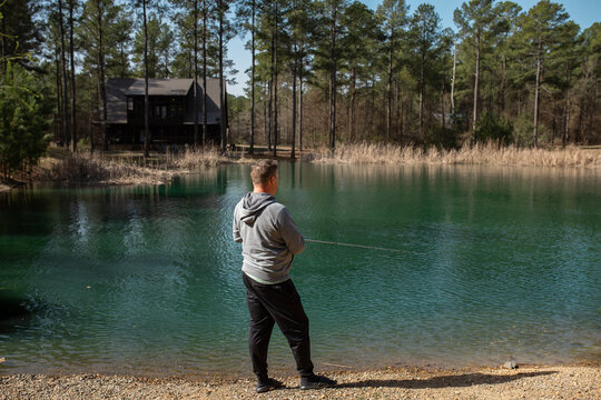 back view of a man fishing a forested pond on a sunny day