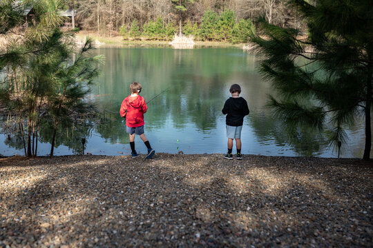 Two boys fishing at a rocky lakeshore surrounded by trees