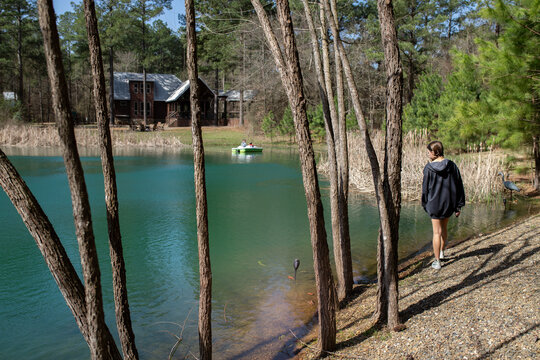Girl walking by lakeshore near cabin with boaters on the water